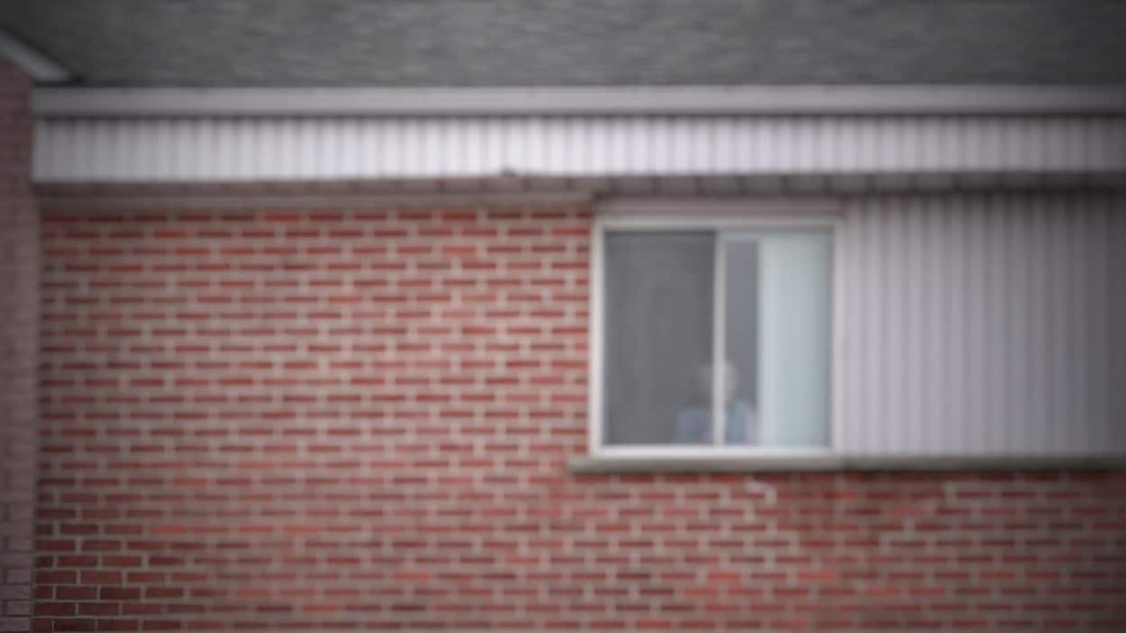 Une personne aînée regarde par sa fenêtre de sa résidence.