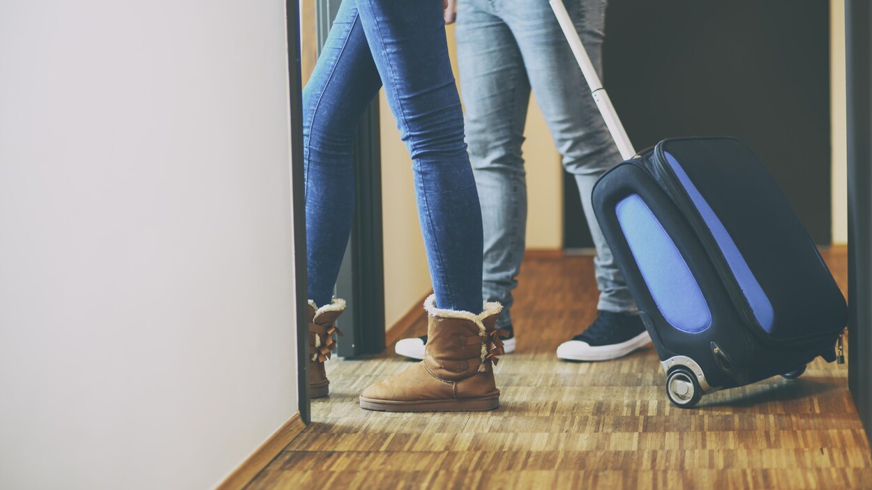 Les jambes d'un couple entrant dans une chambre avec une valise.