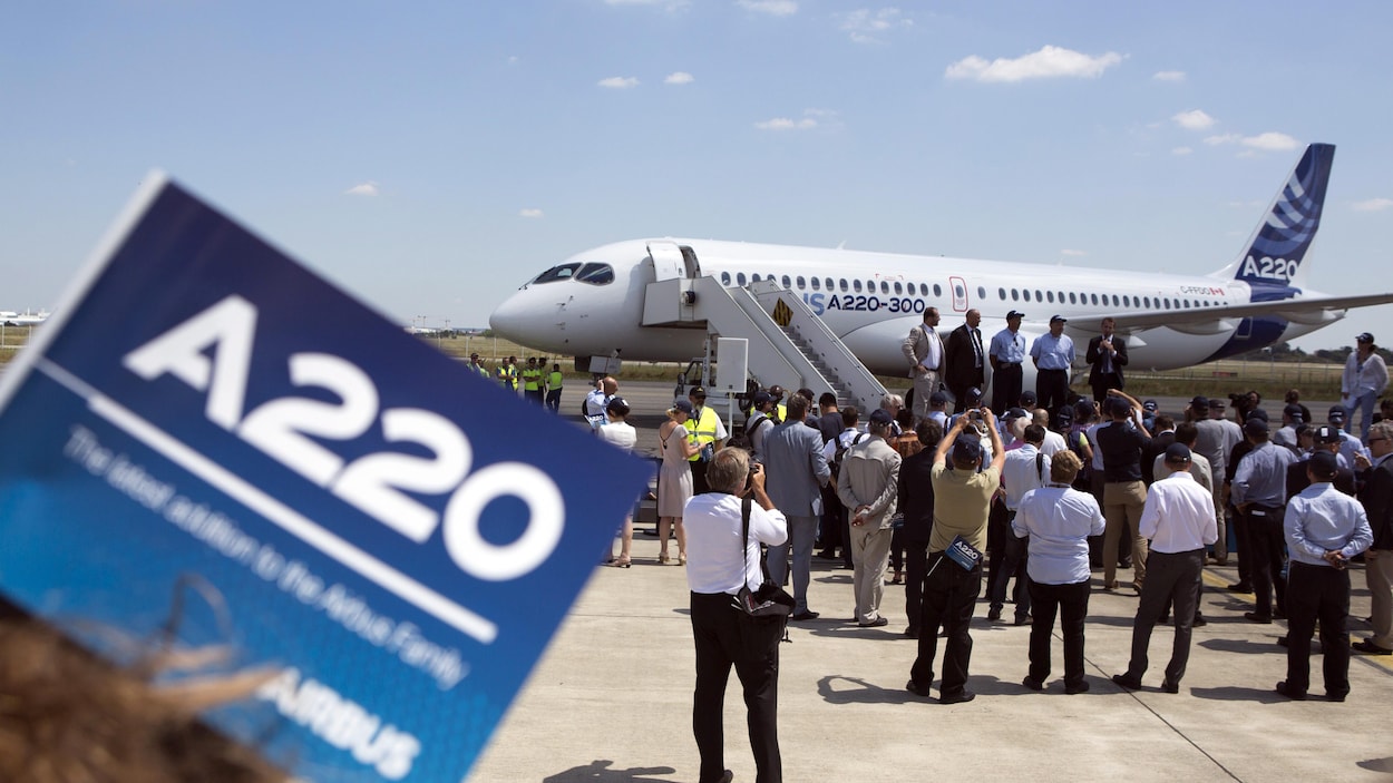 Des membres des médias prennent des images d'un avion A220 sur un tarmac.