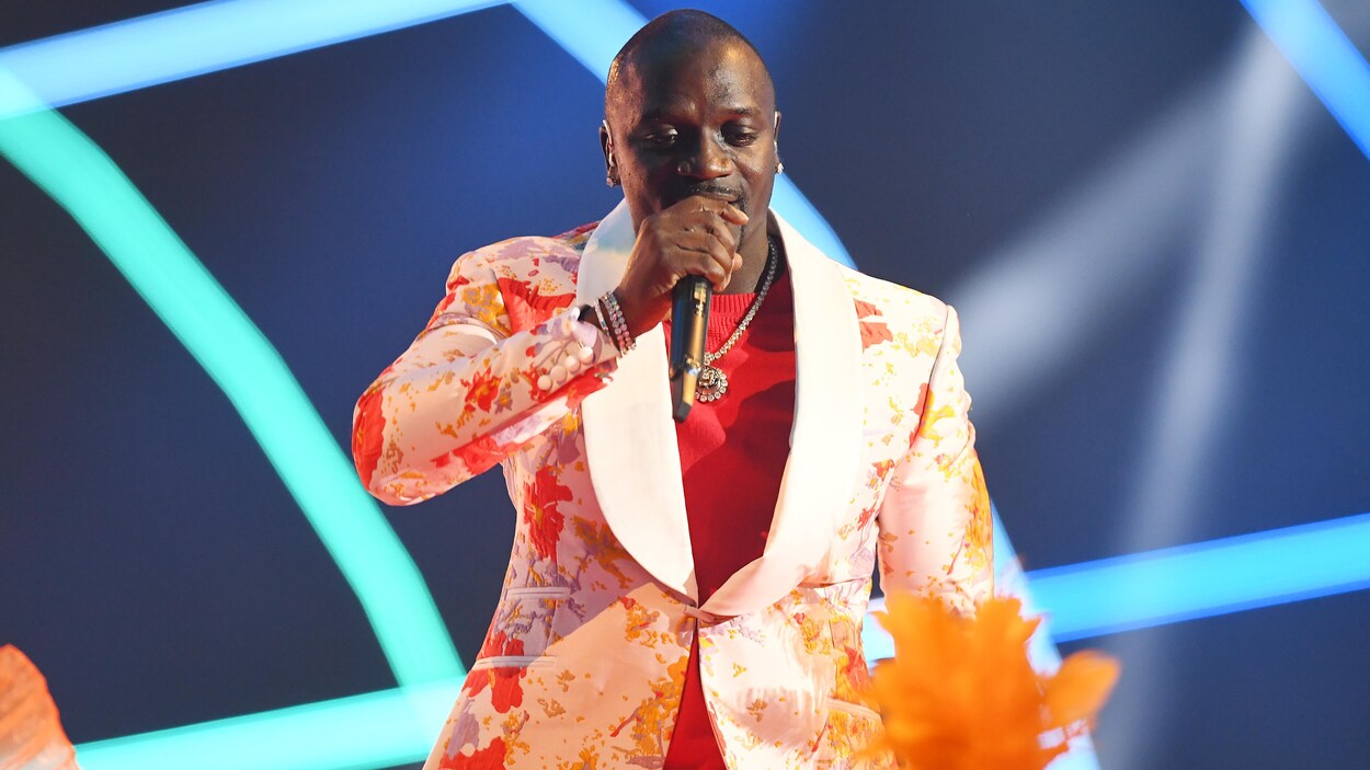 L'homme habillé d'un costume blanc et orange tient un micro et chante.
