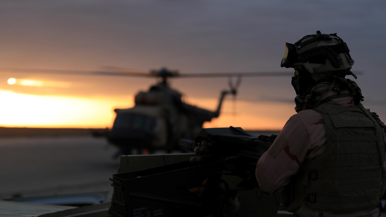 Un soldat regarde au loin. Un hélicoptère est au sol derrière lui.