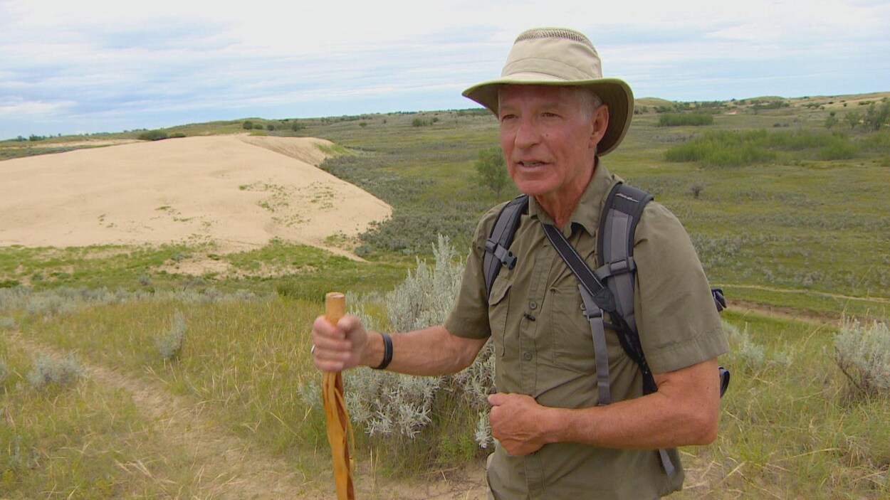 Alain Clermont a un bâton dans la main et un sac au dos pour faire une promenade dans une prairie.