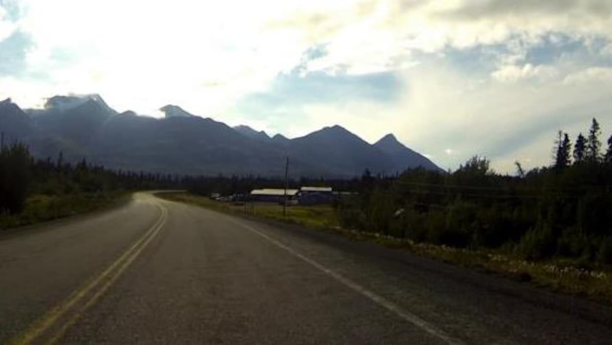 Une route rejoint l'horizon, au coeur d'un paysage nordique et montagneux.