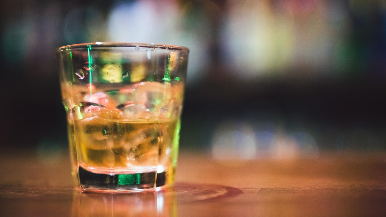 Gros plan sur un verre avec de l'alcool sur des cubes de glace déposé sur une table en bois.