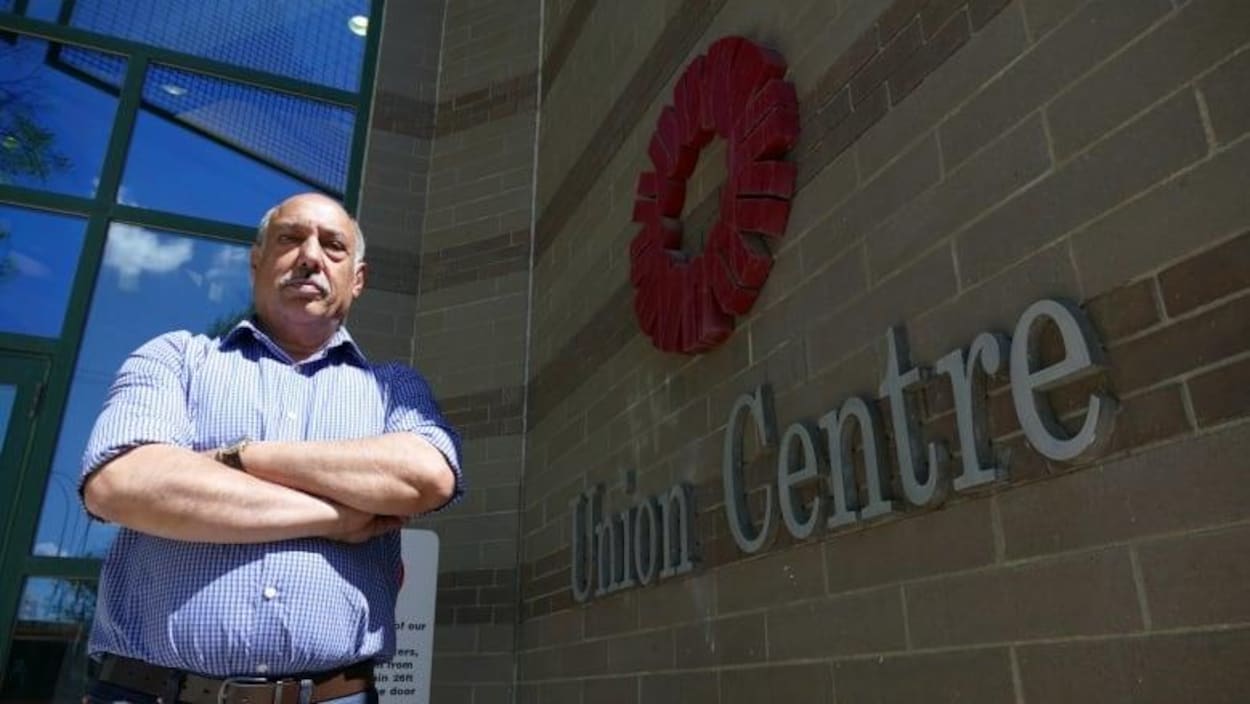 Un homme pose les bras croisés devant un bâtiment.