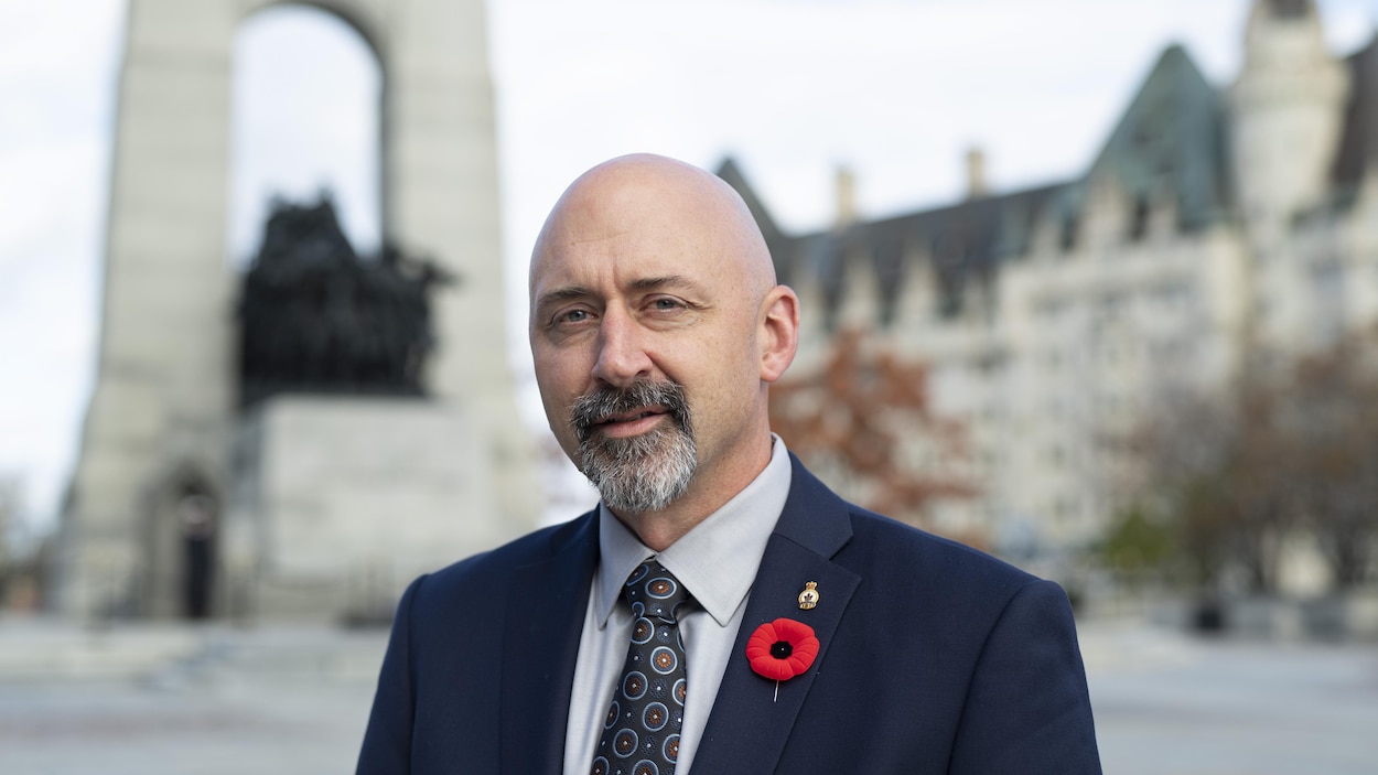 Alex Ruff devant le Monument commémoratif de guerre du Canada à Ottawa, alors qu'il porte un veston bleu et un coquelicot rouge.