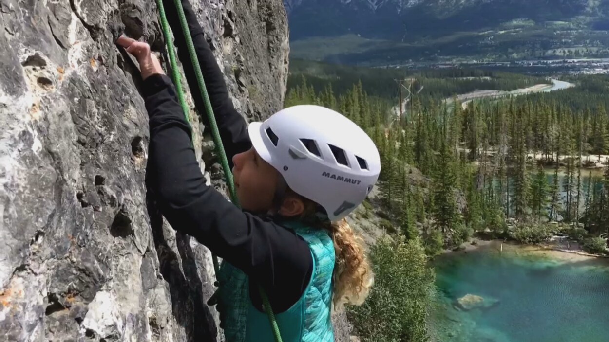 Alexa grimpe sur une falaise avec derrière elle la montagne