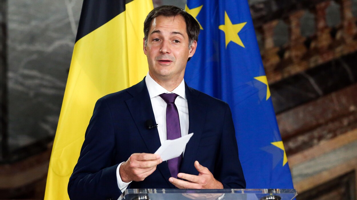 Un politicien s'adresse aux journaliste devant des drapeaux de la Belgique et de l'Union européenne.