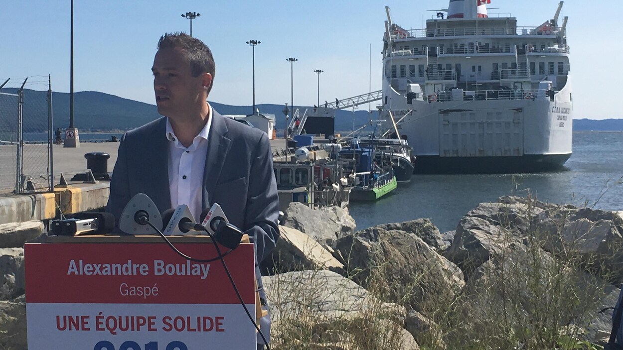 Alexandre Boulay derrière un lutrin avec un bateau en arrière-plan