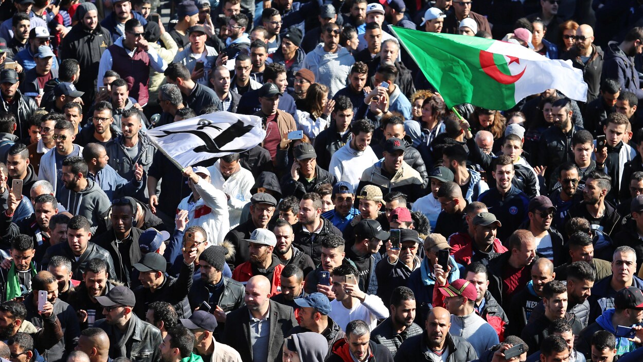 Des personnes marchent dans une rue, certaines brandissant des drapeaux.