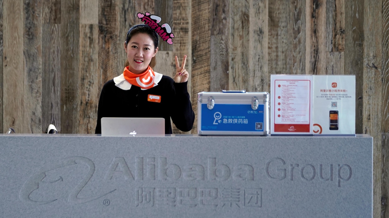 Une employée d'Alibaba, debout derrière un bureau, fait un signe de paix avec la main gauche.
