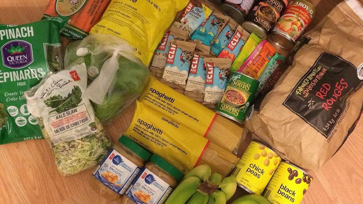 Plusieurs aliments alignés sur le sol pour une photo, comme des bananes, des pâtes, du beurre d'arachide et des barres tendres.