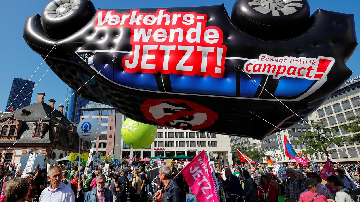 Des manifestants se tiennent en dessous d'une voiture gonflable flottant dans les airs.