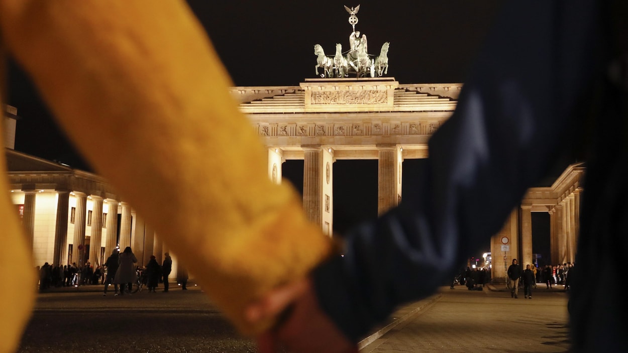 Deux personnes se tiennent la main devant la porte de Brandebourg à Berlin, le soir.