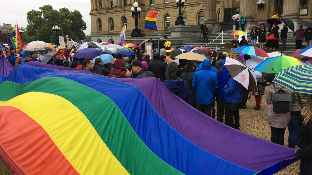 Des gens sont réunis tenant des drapeaux arc-en-ciel