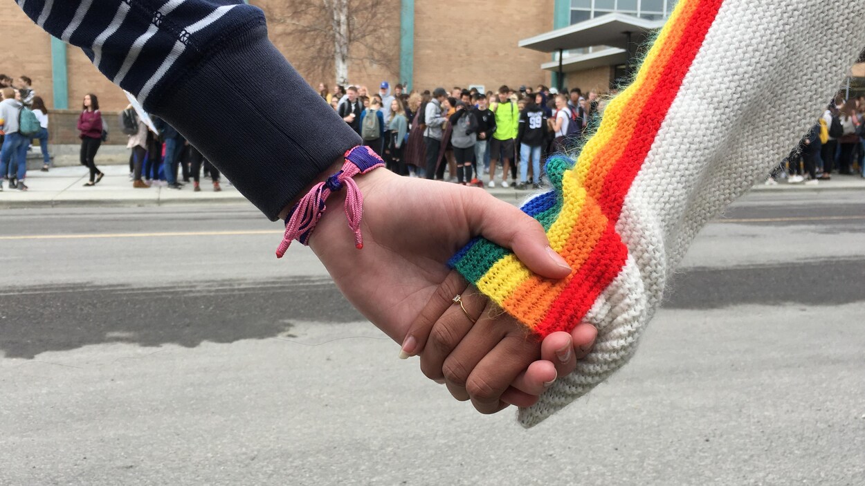 Deux personnes se tiennent par la main. Une porte un chandail aux couleurs de l'arc-en-ciel.