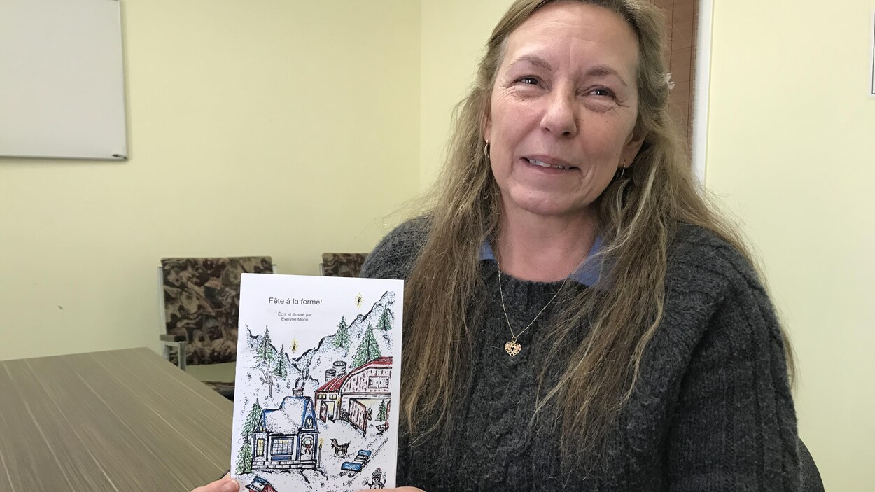 Une femme tient un livre dans ses mains, souriant à la caméra.