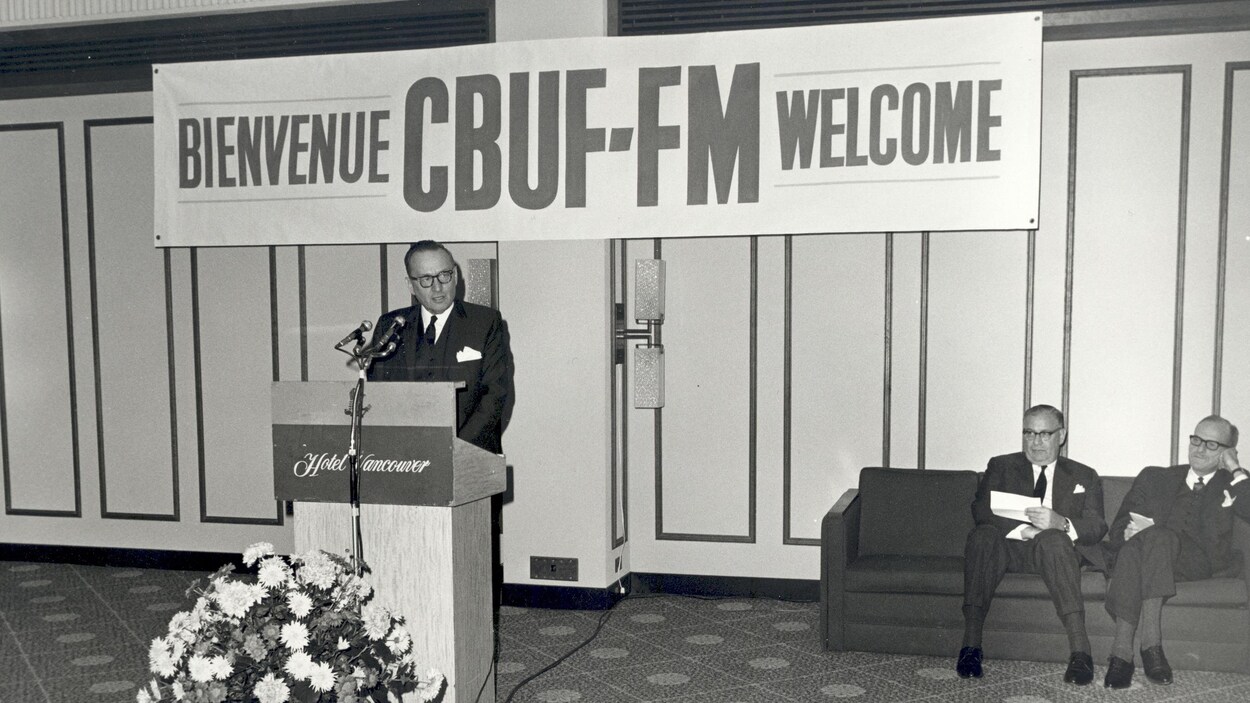 Le président au lutrin prononce un discours. Une banderole à l’arrière indique «Bienvenue CBUF-FM Welcome».