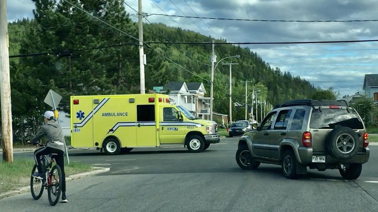 Une ambulance dans une rue qui bloque une voiture et des cyclistes.