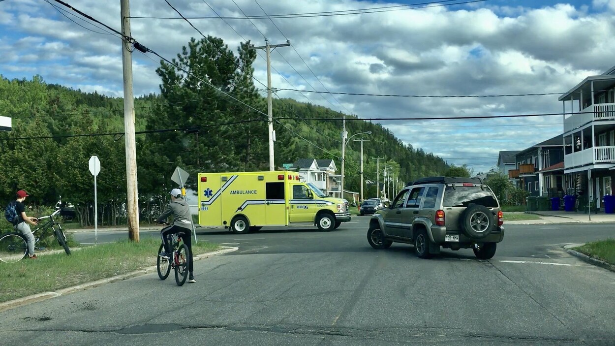 Une ambulance dans une rue qui bloque une voiture et des cyclistes.