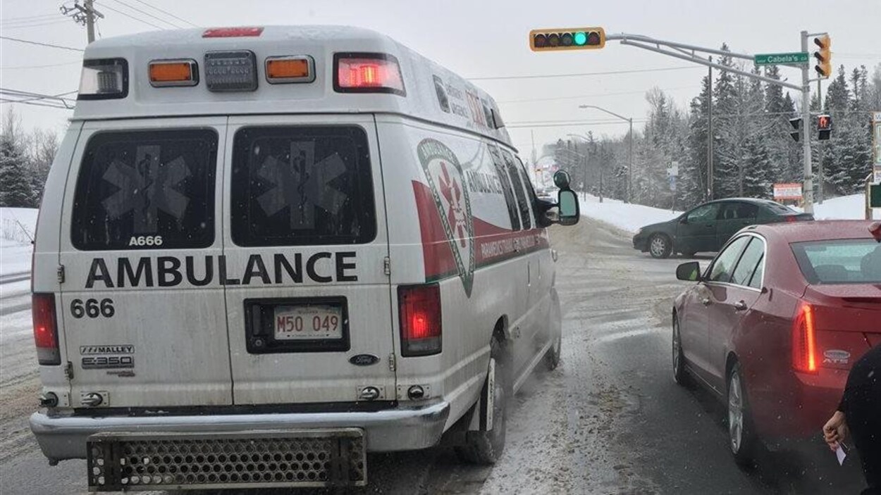 Une ambulance, en hiver, est arrêtée près d'une voiture rouge.