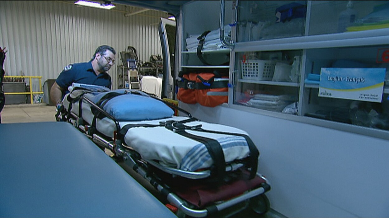 Un ambulancier porte un brancard vide dans une ambulance.