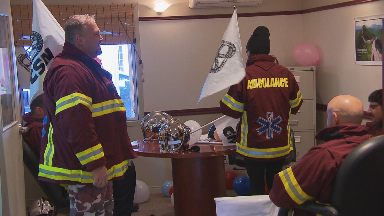 Ambulanciers en uniforme dans un bureau avec des drapeaux de la CSN.