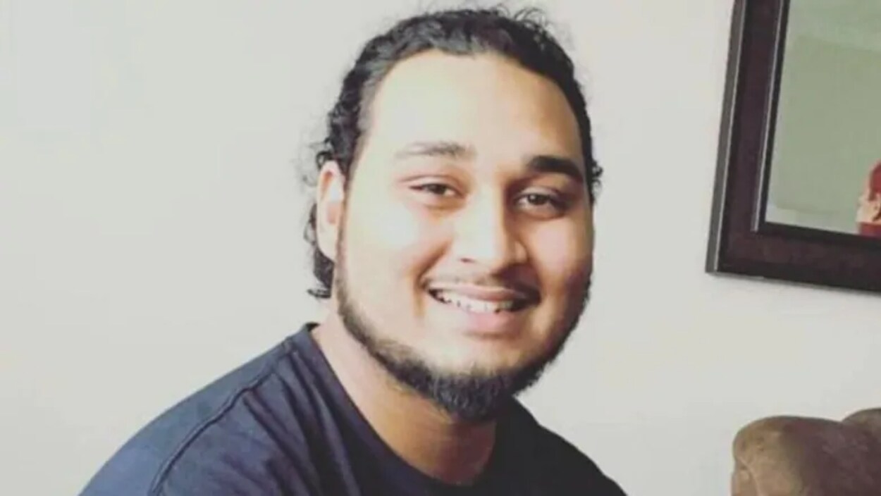 Un homme avec un chandail noir et une barbe.
