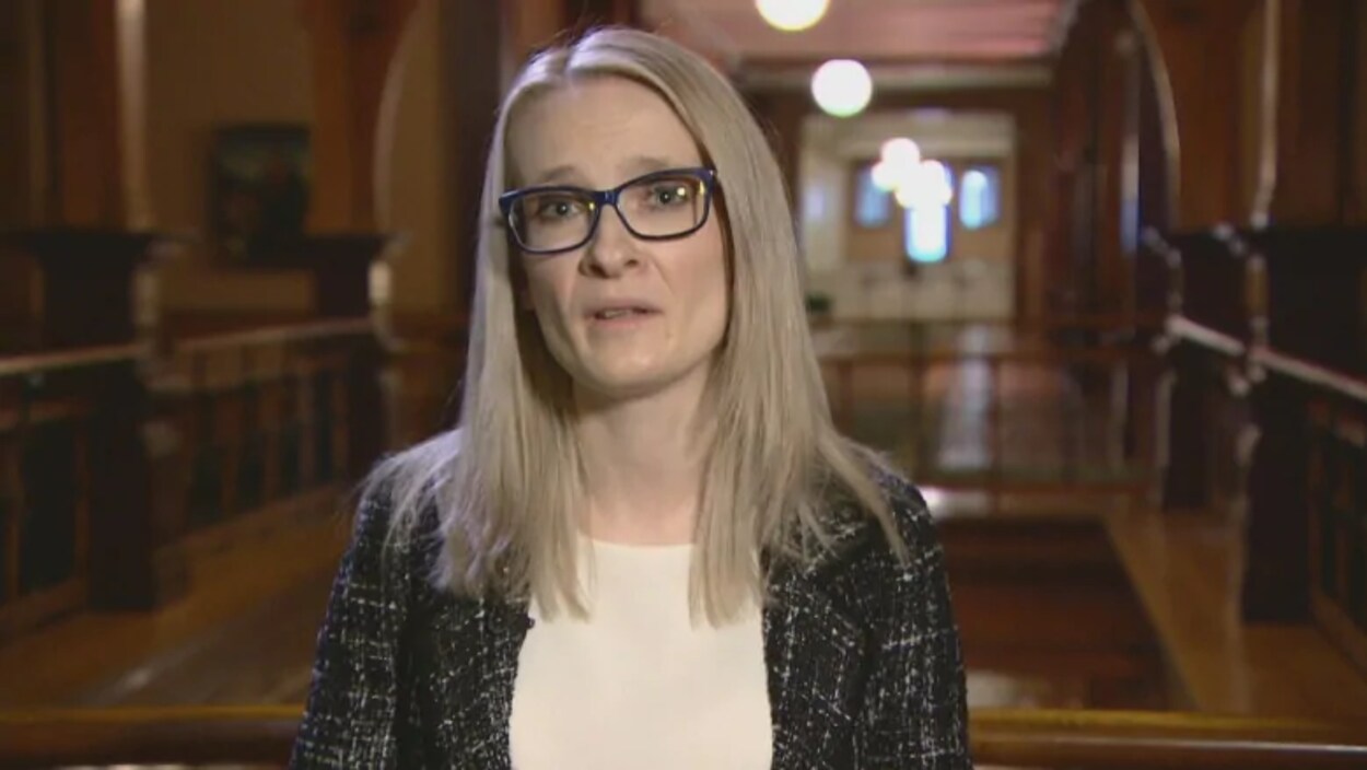 Une femme parle en face de la caméra dans une salle de l'Assemblée législative.