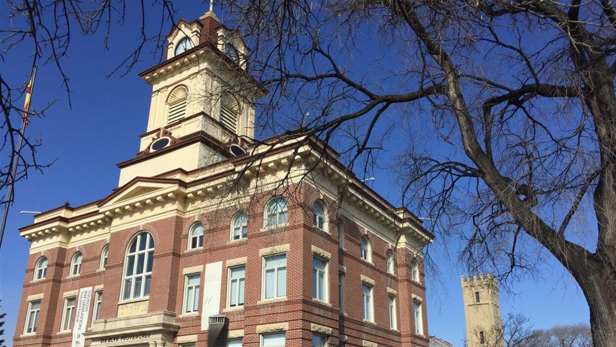 Façade d'un bâtiment patrimonial encadrée par des arbres sans feuilles.