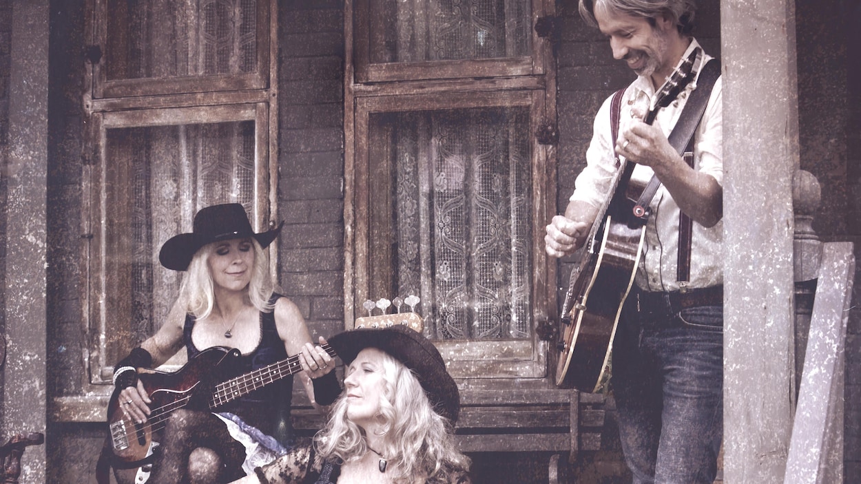 André Lavergne, Annette et Michelle Campagne jouent de la guitare sur le porche d'une maison.