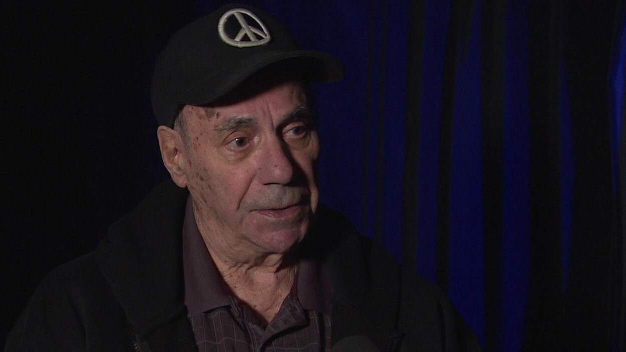 Un homme âgé et portant une casquette parle en entrevue.