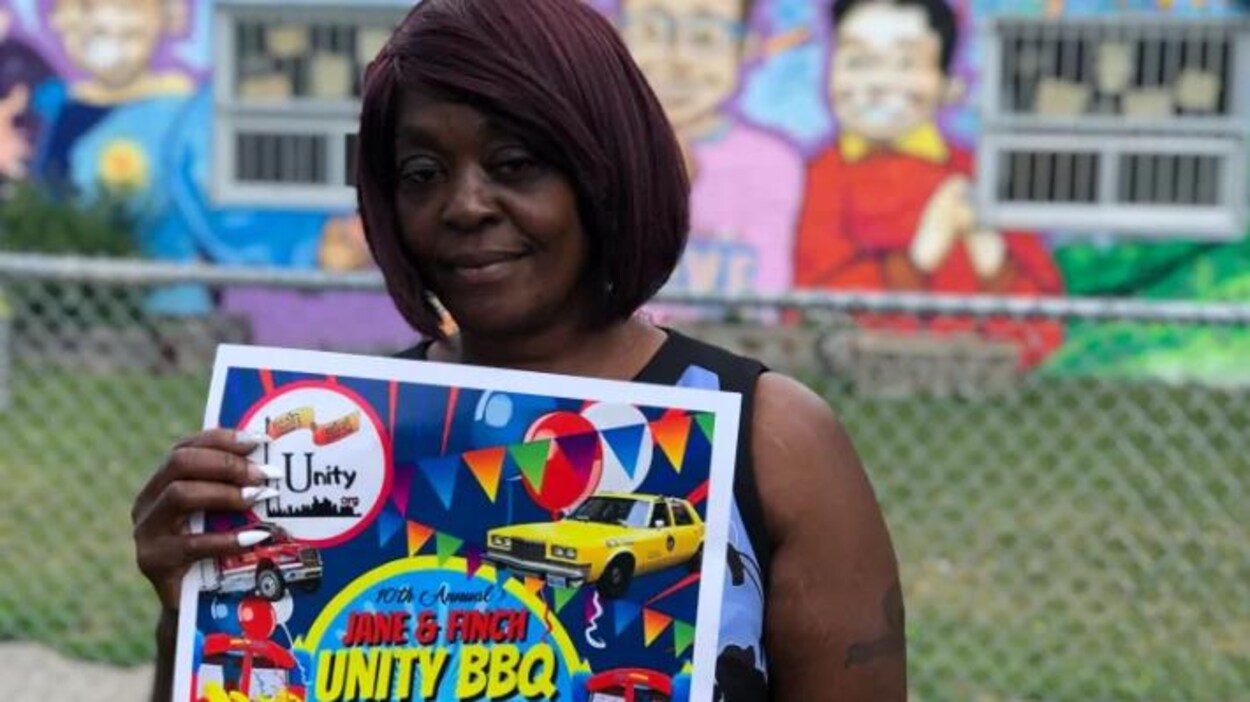 Andrea Tabnor tient une pancarte du barbecue Unity très colorée entre ses mains, elle a les cheveux noirs.