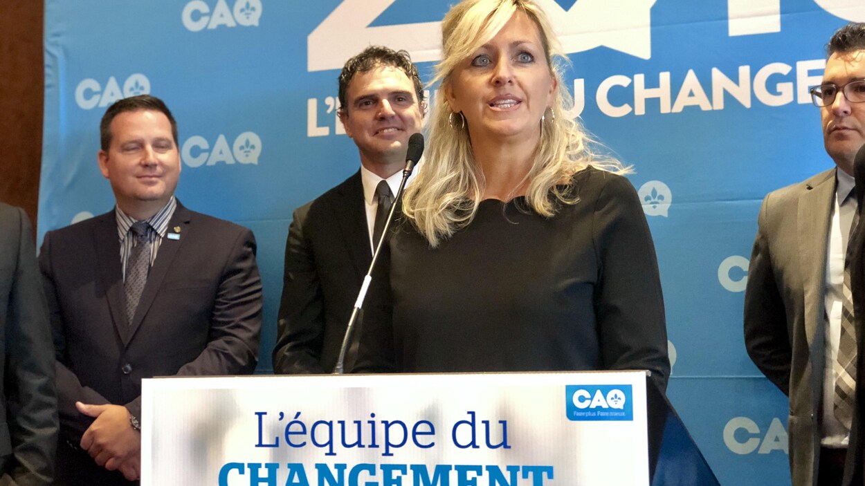 Une femme discute à un lutrin. Elle est entourée de trois candidats de la CAQ.