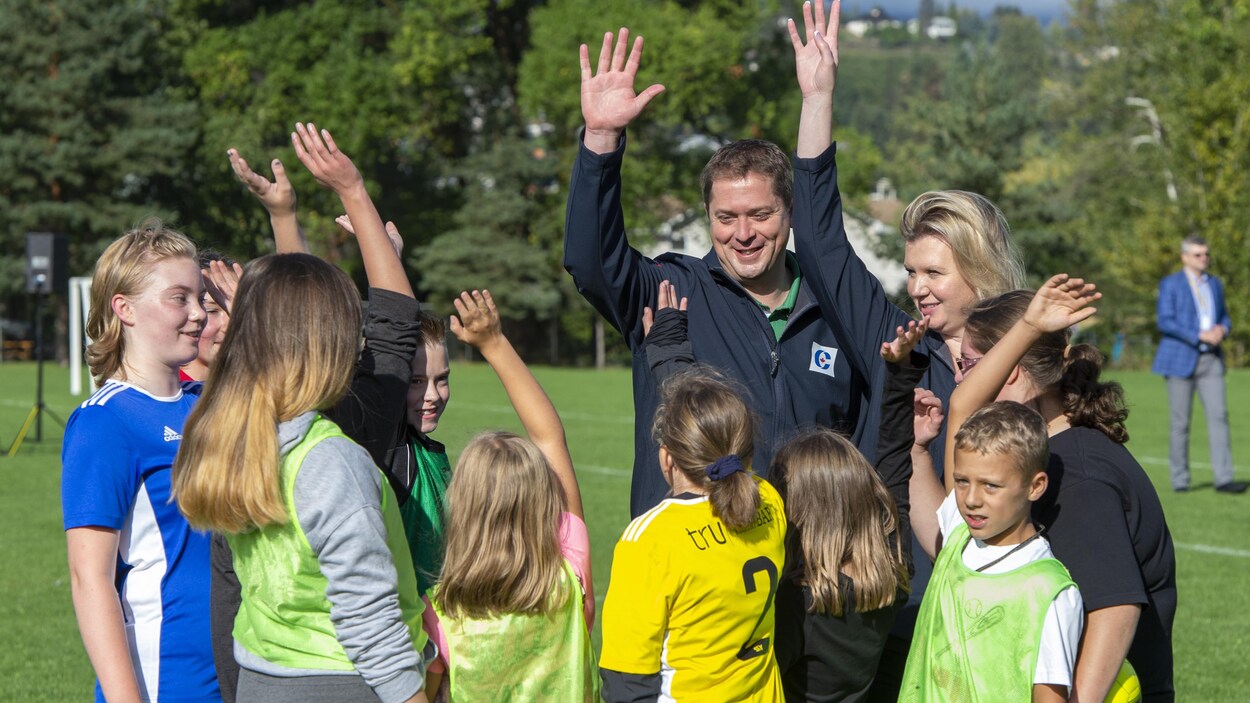 Andrew Scheer, sa femme et des enfants ont une main en l'air, comme s'ils faisaient un cri d'équipe.