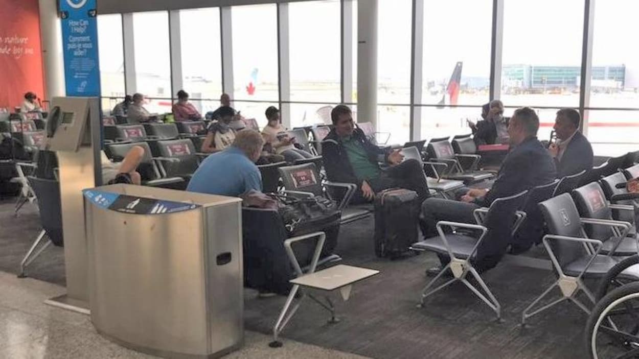 Quatre hommes sont assis dans une zone d'attente. Ils respectent la distanciation sociale.