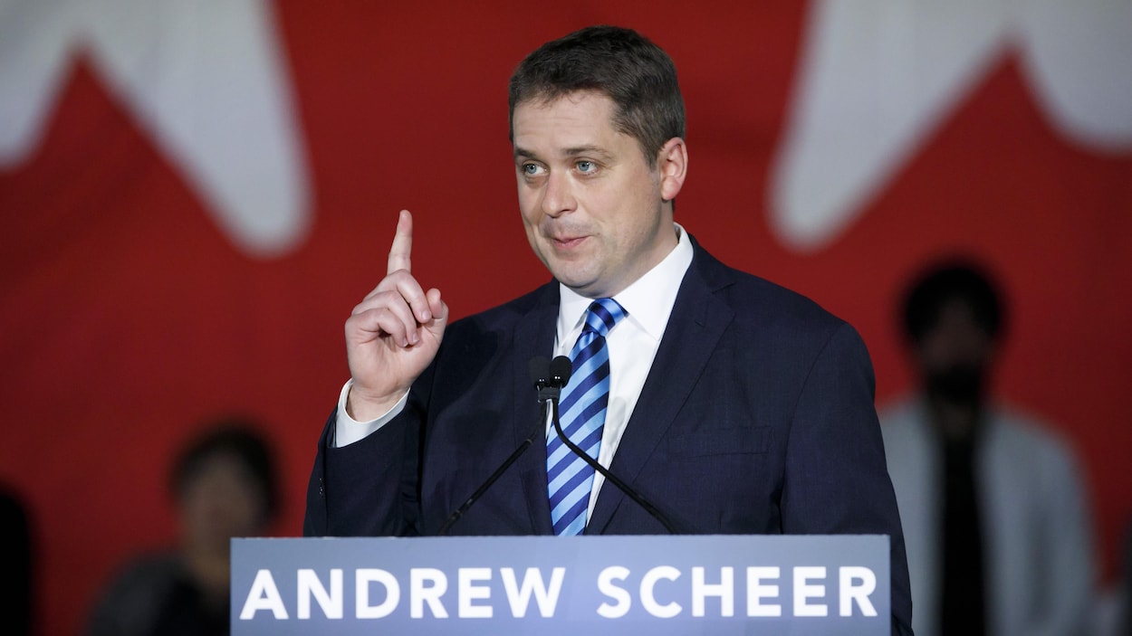 Debout derrière un lutrin, M. Scheer lève le doigt vers le ciel lors d'une allocution publique.
