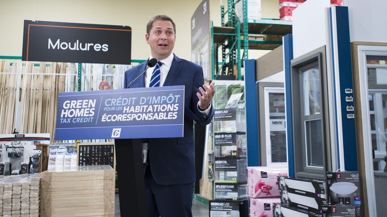 Le chef conservateur fait une annonce devant des planches de bois, dans une quincaillerie.