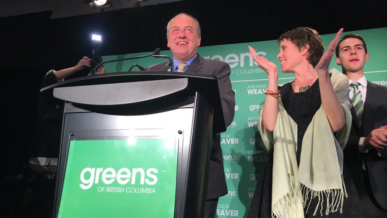 Andrew Weaver est acoudé à un pupitre sur une scène d'où il fait un discours. La députée verte Sonia Furstenau se tient à côté de lui et applaudit.