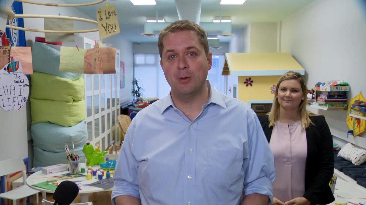 Andrew Scheer s'adresse aux médias. Derrière lui, une femme l'écoute.