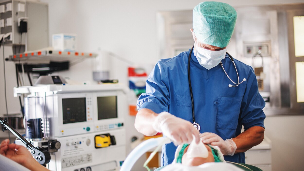 Un anesthésiste place un masque par-dessus le visage d'un patient allongé sur une table de bloc opératoire.