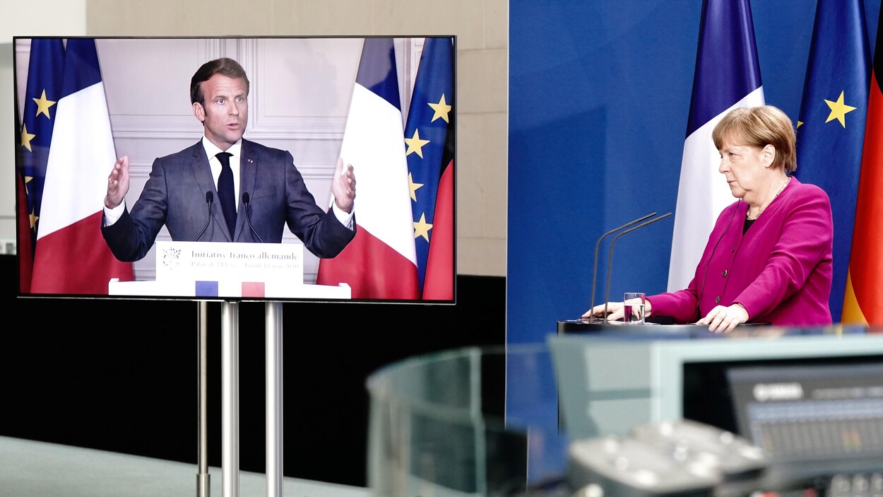 Angela Merkel est devant un lutrin et Emmanuel Macron sur un écran.