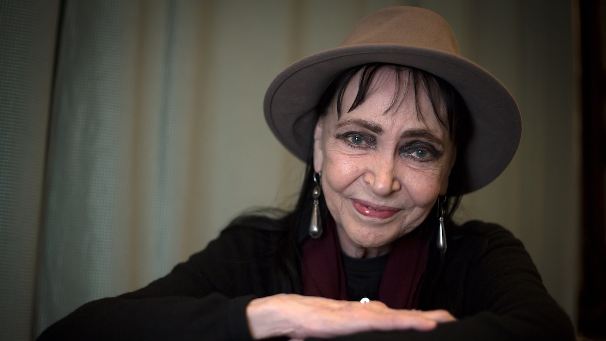 Une femme souriante, aux yeux bleus, porte un chapeau.