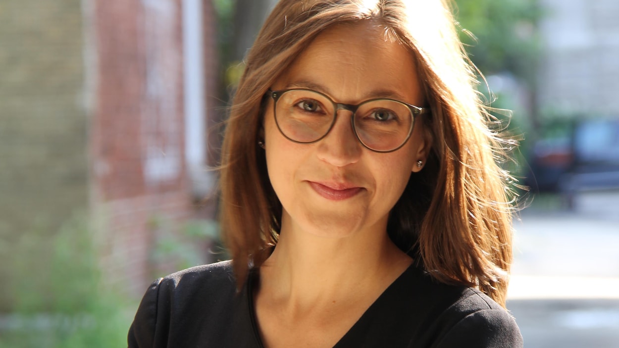 Portrait en couleur, en extérieur, d'Anne-Marie Voisard. La jeune femme sourit, bouche fermée. Elle porte des lunettes et une veste noire.