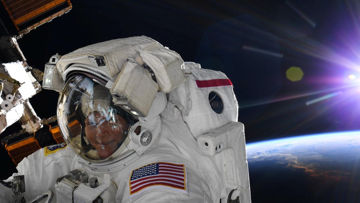Dans sa combinaison d'astronaute, Anne McClain sourit à la caméra, avec la Terre en arrière-plan.