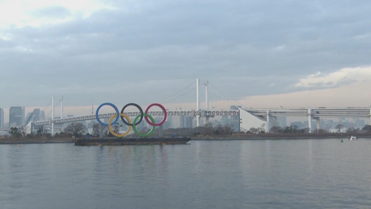 Les cinq anneaux olympiques sont sur une barge devant un grand plan d'eau.