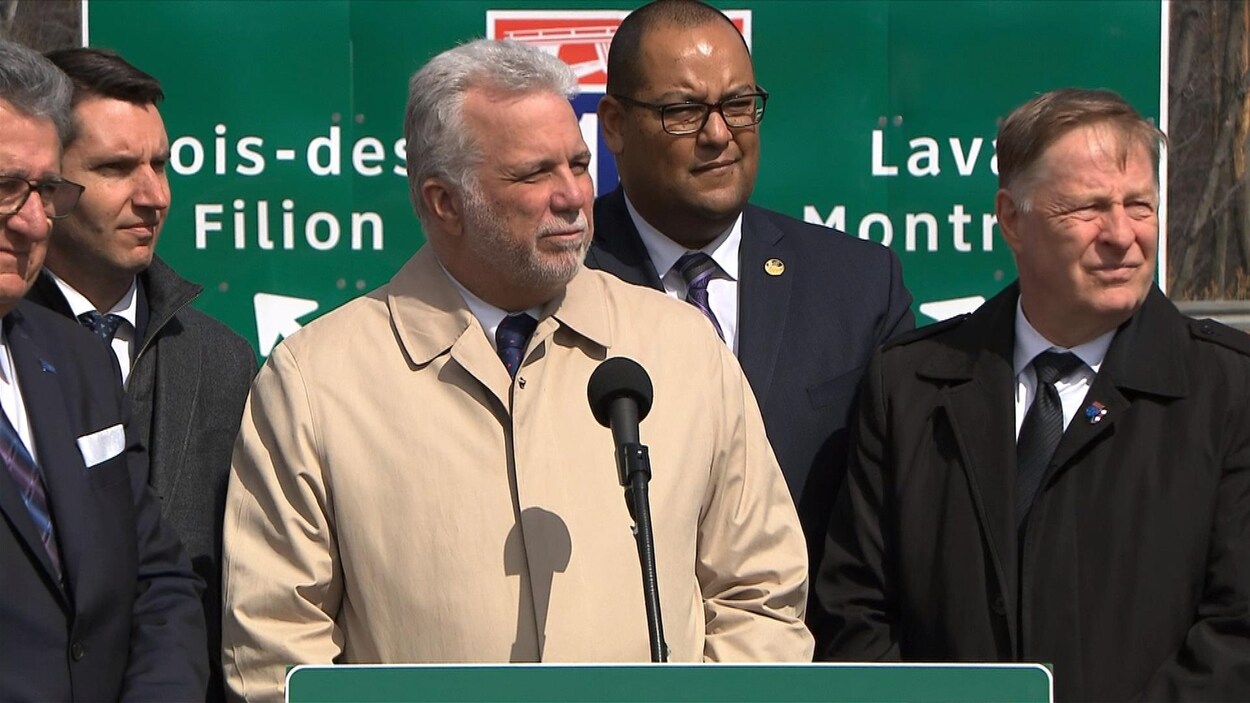 Philippe Couillard et des élus devant un panneau de l'autoroute 19. Philippe Couillard et des élus devant un panneau de l'autoroute 19.