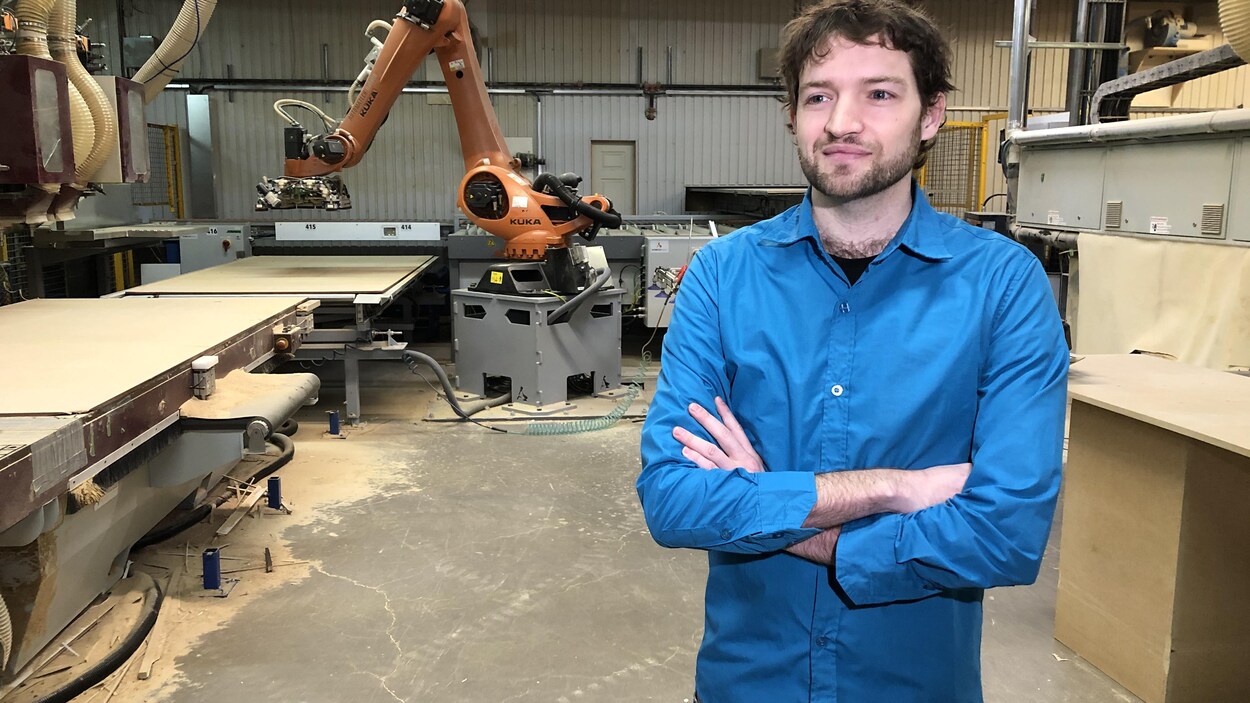 Un homme pose dans une usine, les bras croisés