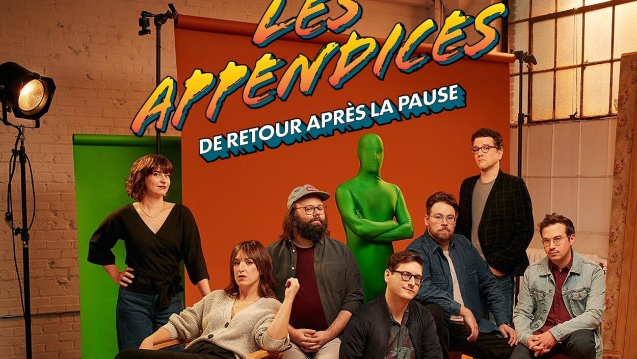 Quatre hommes et deux femmes posent à côté d'une personne habillée d'une combinaison verte de la tête aux pieds.