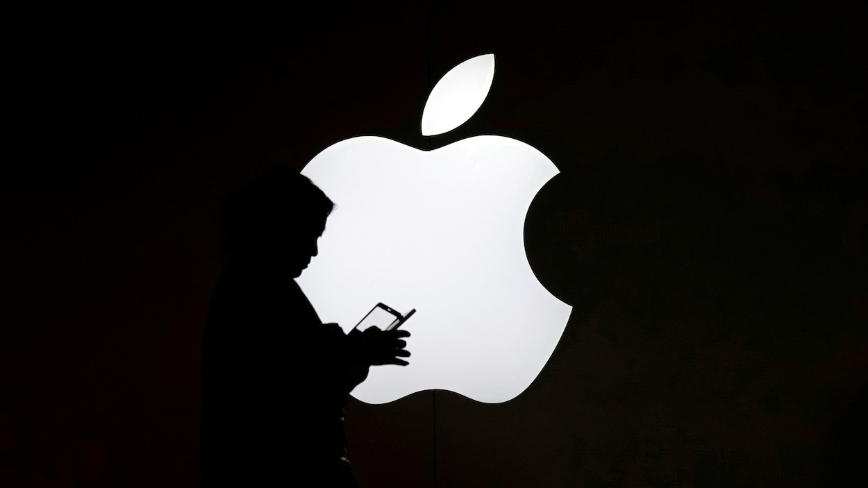 Une femme regarde l'écran de son téléphone portable devant un logo Apple.